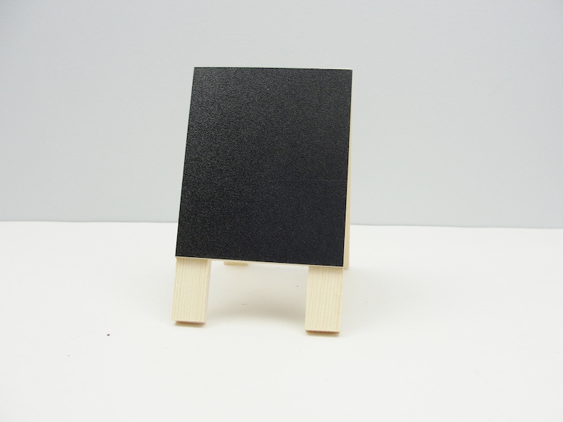 May include: A small black chalkboard easel with wooden legs. The chalkboard is blank and ready for writing.