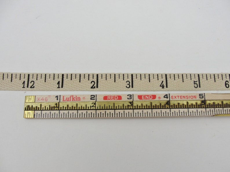 Puede incluir: Una cinta m&eacute;trica de tela blanca con marcas negras y una cinta m&eacute;trica retr&aacute;ctil de madera con marcas negras y texto rojo que dice "Lufkin", "RED", "END" y "EXTENSION".