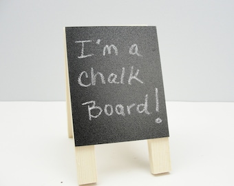 Puede incluir: Un pequeño caballete de pizarra negra con las palabras "I'm a chalk board!" escritas con tiza blanca.