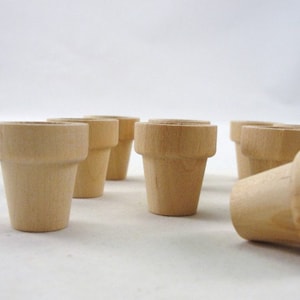 May include: A set of eight small, unfinished wooden flower pots. The pots are all the same size and shape, and they are made of natural wood.