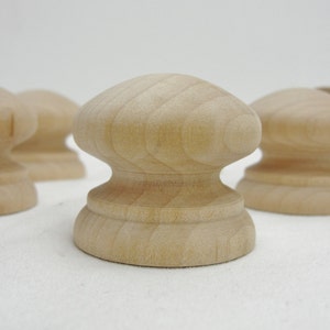 May include: Four unfinished wooden knobs with a rounded top and a slightly raised base. The knobs are made of light-colored wood and have a smooth, polished finish.