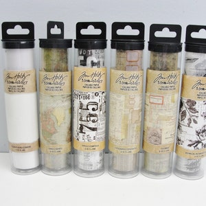 May include: Six clear plastic tubes with black lids and hanging loops, each containing a roll of patterned paper. The paper is printed with various designs, including maps, typography, and botanical illustrations. The tubes are labeled "Jim  Holt  idea-ology  Collage Paper  Papier de Collage".