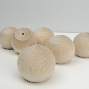 May include: Six unfinished wooden balls, each with a smooth, natural wood finish. The balls are arranged in a semi-circle on a white surface.