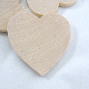 May include: A set of six unfinished wooden heart shapes. The hearts are made of natural wood and have a smooth surface.