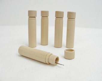 May include: Five small wooden tubes with a round top and a small hole at the bottom. One tube is lying on its side with a needle sticking out of the hole.