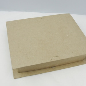 May include: A square, light brown cardboard box with a flat top surface and a slightly wider base. The box is constructed from plain, unprinted fiberboard material with a visible texture, featuring clean edges and a simple, functional design.