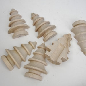May include: Six unfinished wooden Christmas tree ornaments. The ornaments are all different sizes and shapes, and they are all made of a light-colored wood.