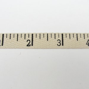 Puede incluir: Una cinta m&eacute;trica de tela beige con marcas negras. La cinta muestra medidas de 1 a 4 pulgadas (aproximadamente 2,5 a 10 cm).