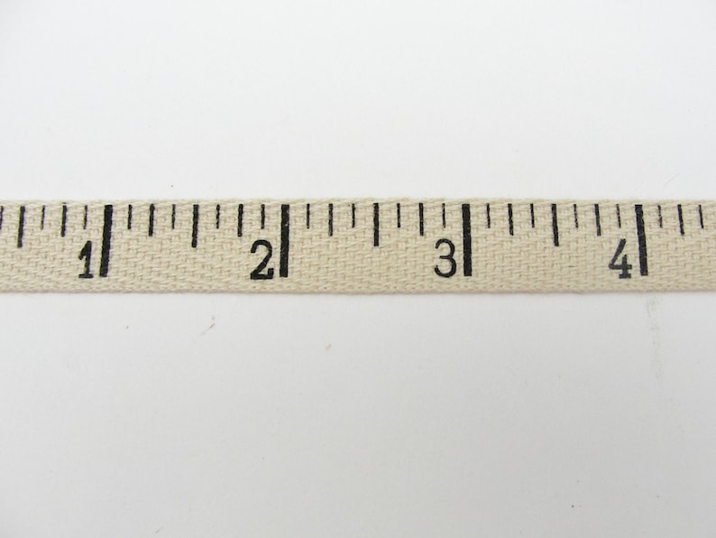 Puede incluir: Una cinta m&eacute;trica de tela beige con marcas negras. La cinta muestra medidas de 1 a 4 pulgadas (aproximadamente 2,5 a 10 cm).