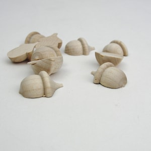 May include: A group of eight unfinished wooden acorn shapes, some with the top half removed, on a white surface.