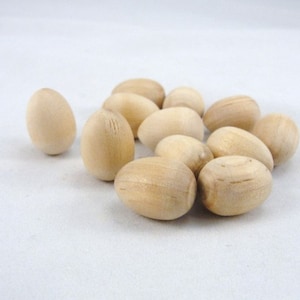 May include: A group of 10 natural wood eggs, each with a smooth, slightly textured surface. The eggs are arranged in a loose pile on a white background.