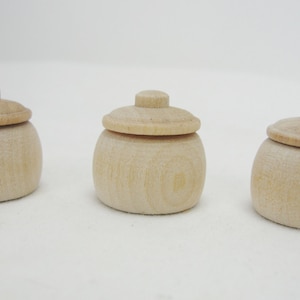 May include: Three small wooden jars with lids. The jars are unpainted and have a natural wood finish.