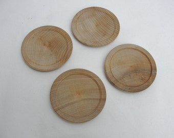 May include: Four wooden coasters with a natural wood finish. The coasters are round and have a slightly raised edge.