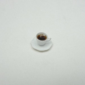 May include: A white teacup and saucer with a brown liquid inside the cup.