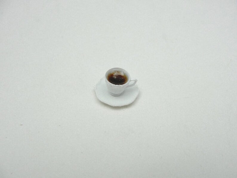 May include: A white teacup and saucer with a brown liquid inside the cup.