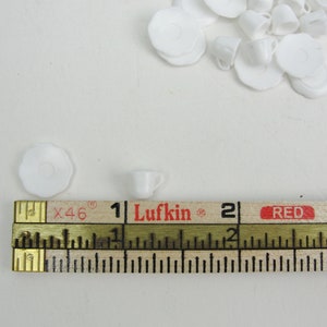 May include: A white ceramic teacup and saucer set, measuring approximately 1 inch in diameter, next to a wooden ruler marked with the brand "Lufkin" and the numbers 1, 2, and 3.