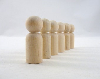 May include: A row of seven unfinished wooden peg dolls, standing in a line on a white surface. The dolls are all the same size and shape, with round heads and cylindrical bodies.
