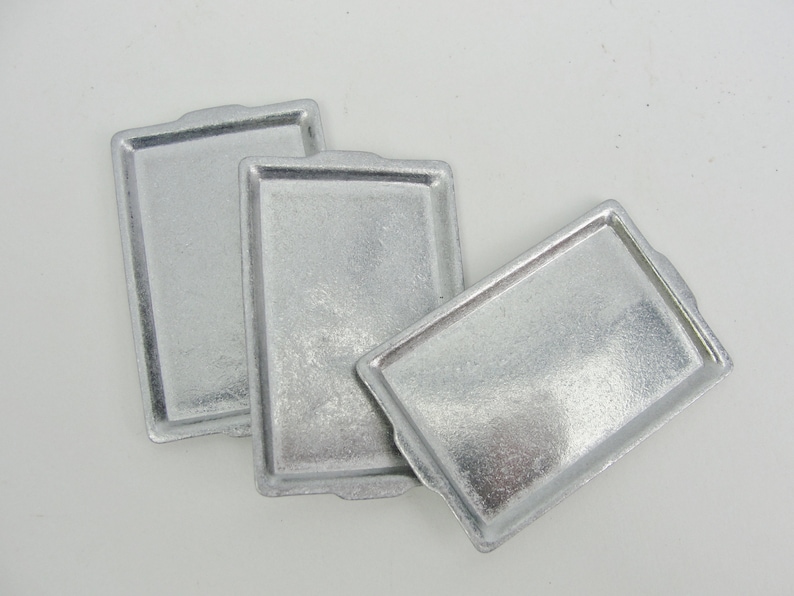 May include: Three silver baking sheets, each with a slightly different shape and size.