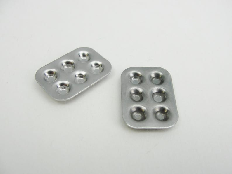 May include: Two silver baking pans with six round depressions each. The pans are made of metal and have a shiny finish.