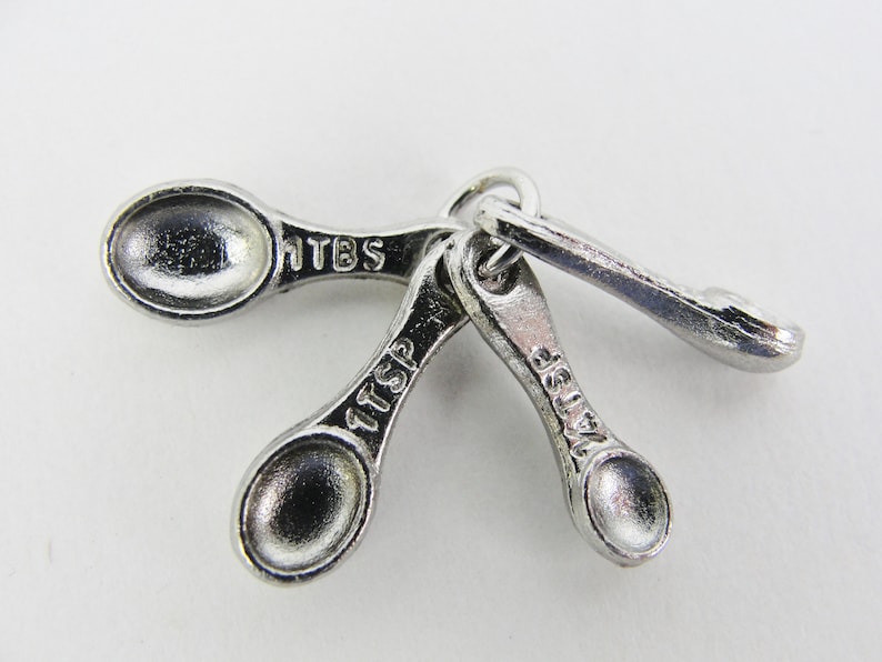 May include: A set of three silver measuring spoons with the measurements 1 tbsp, 1 tsp, and 1/4 tsp.