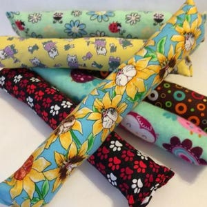 May include: Six colorful catnip toys made of fabric with different patterns. The toys are shaped like long cylinders and are filled with catnip. The patterns include sunflowers, paw prints, ladybugs, and polka dots.
