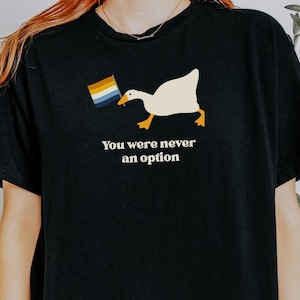 Op de afbeelding: Zwart T-shirt met een witte gans die een regenboogvlag vasthoudt en de tekst "You were never an option".