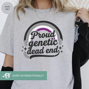 May include: Sport grey t-shirt with a graphic that reads "Proud genetic dead end" in a stylized font. The design includes a rainbow-like arch with purple, gray, and black colors. The shirt is a casual wear item.