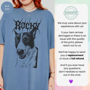 May include: Blue jean-coloured t-shirt with a black and white dog portrait and the name "Rocky" in a gothic font. The shirt has a relaxed fit and short sleeves. The image includes a guarantee badge and customer service text.