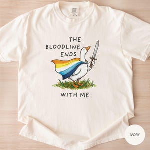 May include: Ivory-colored t-shirt featuring a cartoon goose with a sword and a cape in yellow, orange, blue, and white. Text on the shirt reads "THE BLOODLINE ENDS WITH ME."