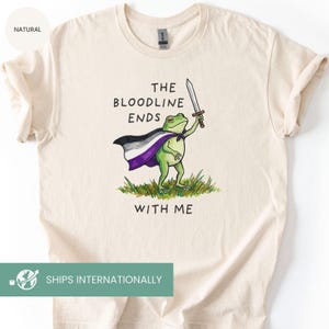 May include: Cream-colored t-shirt featuring a green frog wearing a cape with the asexual pride flag colors and holding a sword. The text "THE BLOODLINE ENDS WITH ME" is printed above and below the frog illustration.