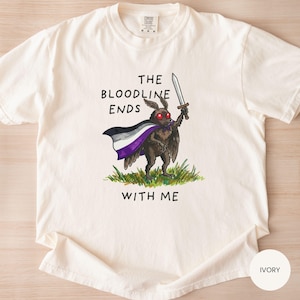 May include: Ivory-colored t-shirt featuring a cartoon moth holding a sword and wearing a cape with the asexual pride flag colors. The text "THE BLOODLINE ENDS WITH ME" is printed above and below the moth illustration.