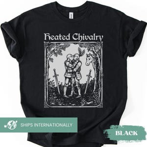 Puede incluir: Una camiseta negra de manga corta con un estampado gráfico blanco de dos caballeros con armadura abrazándose y besándose. La ilustración incluye dos espadas, un caballo y árboles, enmarcados con el texto Heated Chivalry arriba.