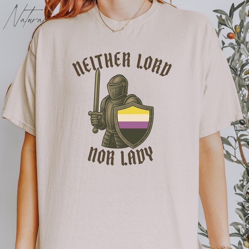 May include: Beige t-shirt with the text "NEITHER LORD NOR LADY" in brown. The shirt features a graphic of a knight holding a sword and shield with the non-binary pride flag colors. The shirt is a casual wear item.