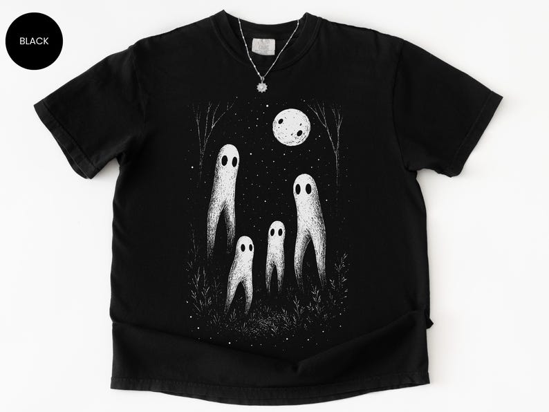 May include: Black t-shirt featuring a whimsical illustration of four white ghost figures under a full moon and starry night sky. The design includes trees and grass, creating a spooky, yet charming scene. A silver necklace with a pendant is visible.