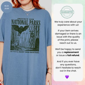 May include: A blue jean-coloured t-shirt with the text "PROTECT OUR NATIONAL PARKS" and "OR WE'LL HAUNT YOUR BACKYARD." The graphic includes a bat, forest, and several creatures. The t-shirt has a loose fit.