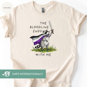 May include: Cream-colored t-shirt featuring a raccoon wearing a cape with the asexual pride flag colors and holding a sword. The text "THE BLOODLINE ENDS WITH ME" is printed above and below the raccoon illustration.