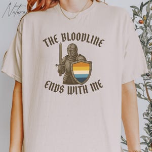 May include: A white t-shirt featuring a graphic of a knight holding a sword and shield. The text "The Bloodline Ends With Me" is printed on the shirt.