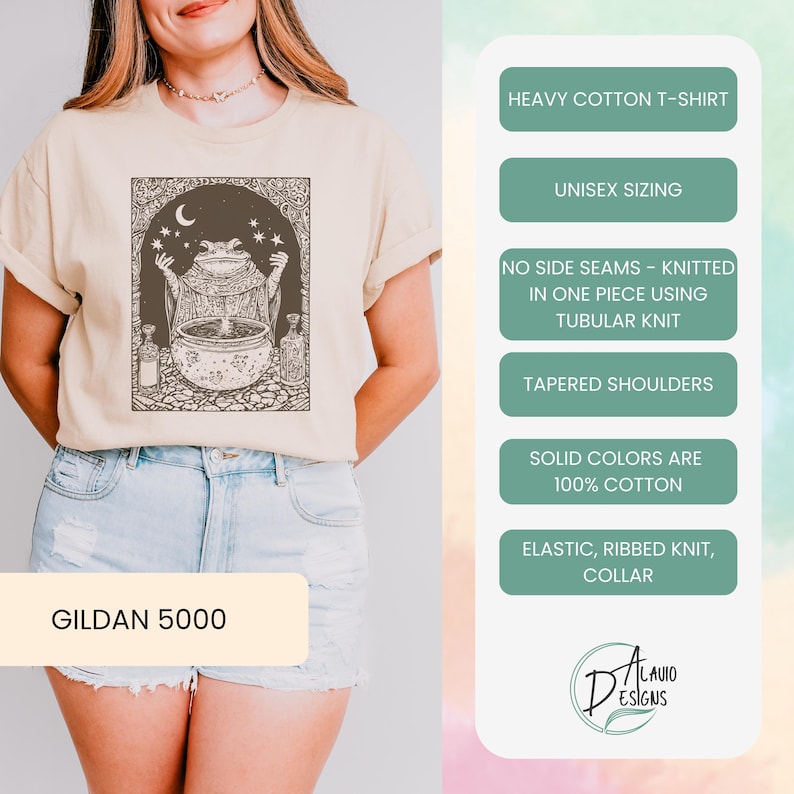 May include: A beige t-shirt with a graphic of a frog holding a cauldron with stars and a crescent moon. The text "GILDAN 5000" is on the bottom of the shirt. The shirt is made of heavy cotton and has a unisex sizing. It is knitted in one piece using tubular knit and has tapered shoulders. The shirt is 100% cotton and has an elastic, ribbed knit collar.