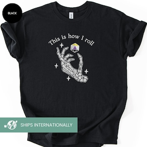 May include: Black t-shirt with the text "This is how I roll" above a skeleton hand holding a multi-sided die. The die has purple, yellow, and white facets. Four white stars surround the hand. The shirt is a Gildan brand.