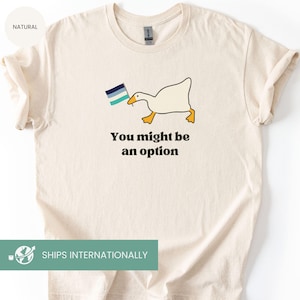 May include: Cream-colored t-shirt featuring a cartoon goose holding a flag with blue and white stripes. The text "You might be an option" is printed below the goose in a bold, black font. The shirt has a crew neck and short sleeves.