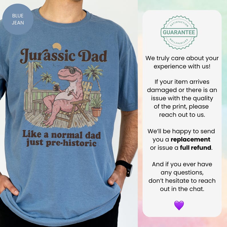 May include: Blue jean t-shirt with a graphic featuring a relaxed dinosaur in sunglasses, the text "Jurassic Dad," and the phrase "Like a normal dad just pre-historic." The design includes palm trees and a wooden deck.