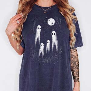 May include: True navy blue t-shirt featuring a whimsical ghost design under a full moon. The graphic includes four white ghost figures, trees, and stars. The shirt is a relaxed fit, perfect for Halloween or spooky season.