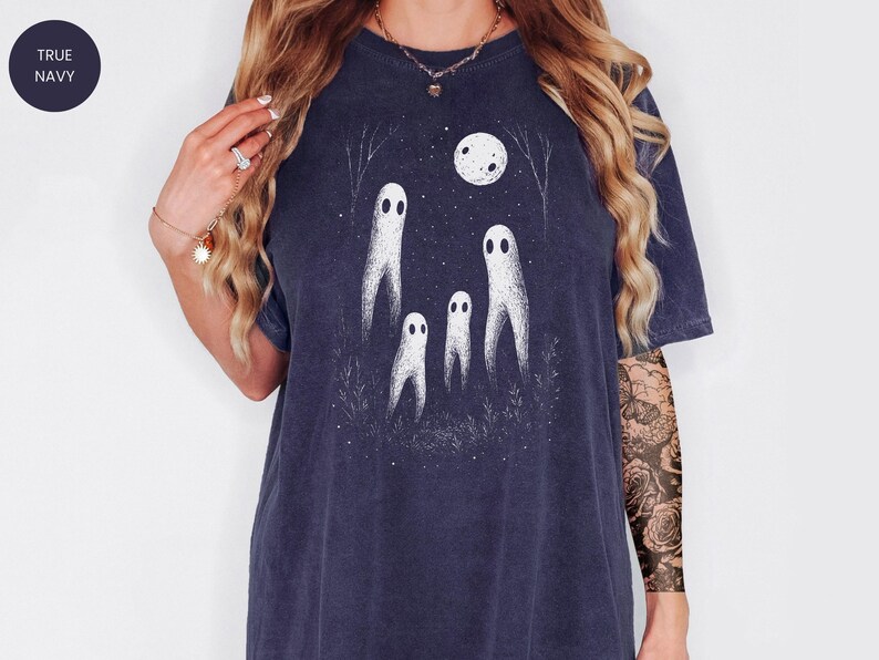 May include: True navy blue t-shirt featuring a whimsical ghost design under a full moon. The graphic includes four white ghost figures, trees, and stars. The shirt is a relaxed fit, perfect for Halloween or spooky season.