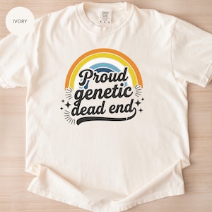 May include: Ivory-colored t-shirt with the text "Proud genetic dead end" in a retro font, set against a rainbow design. The shirt is made of a soft material and has a classic crew neck.
