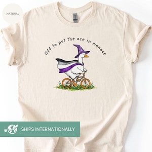 May include: Cream-colored t-shirt featuring a cartoon goose riding a bicycle, wearing a wizard hat and a cape with asexual pride colors. The text "Off to put the ace in menace" is arched above the goose.