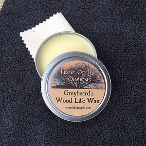 Puede incluir: Una pequeña lata de cera para madera Greybeard's Wood Life Wax de Tree of Life Designs. La lata es plateada con una etiqueta marrón que presenta un árbol y el texto "Tree of Life Designs, Greybeard's Wood Life Wax, treeoflifedesigns.com".