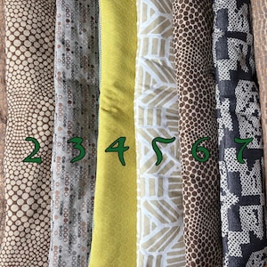 May include: Eight vertical fabric strips arranged side-by-side, labeled with green numbers one through eight. The patterns include brown reptile textures, brown and white polka dots, a solid lime green, and geometric white and brown designs.
