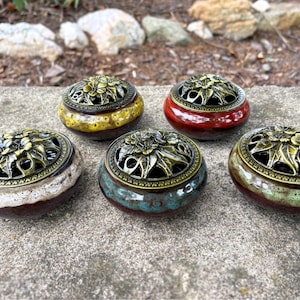May include: Five round ceramic incense burners with glossy, multi-colored glazed finishes. Each burner features a removable, ornate, antique-brass-toned metal lid with a detailed floral and leaf cutout design, allowing for smoke ventilation.