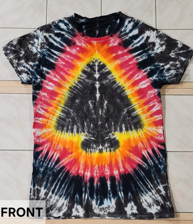 Pu&ograve; includere: Una maglietta tie-dye con un motivo a spirale nero, rosso, arancione e giallo. La maglietta ha un girocollo e maniche corte. La parola "FRONT" &egrave; visibile in basso a sinistra.