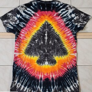Pu&ograve; includere: Una maglietta tie-dye con un design nero, rosso, arancione e giallo. Il retro della maglietta presenta un motivo centrale a forma di freccia. I colori della maglietta si fondono in un effetto a spirale, creando un aspetto unico.